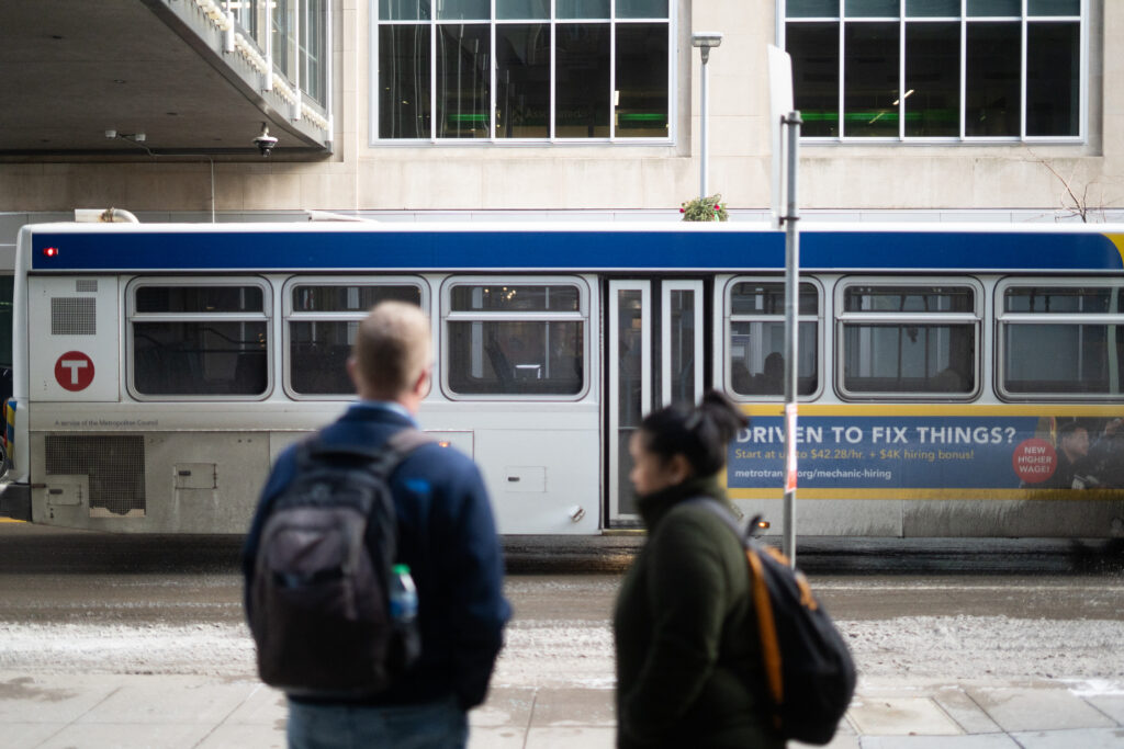 Two people stand in the foreground in front of a Metro Transit bus in downtown Minneapolis